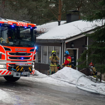 En brandbil på skolvägen i Vanda med brandmän i utrustning i bakgrunden. 