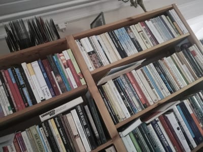 Kuva puisesta kirjahyllystä joka on täynnä kirjoja. Hyllyn päällä on vanhoja äänilevyjä.
