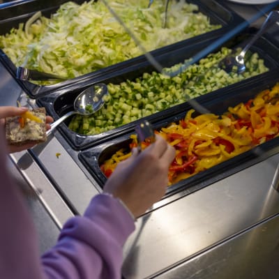 En elev tar strimlad paprika från en salladsbuffé i en skolmatsal.