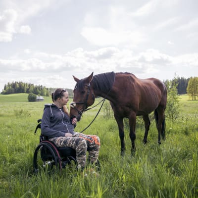 Nicole Hellberg sitter i sin rullstol ute i hagen med sin häst.