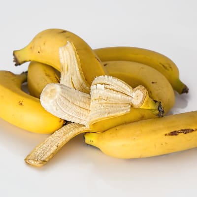 Kuvassa banaaneja, yksi kuorittu auki.