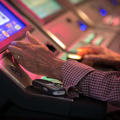 Lähikuva vanhan miehen käsistä pelaamassa rahapelejä Casino Helsingissä.