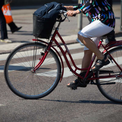 Anonyymi nainen polkee pyörällä kaupungissa kesällä.