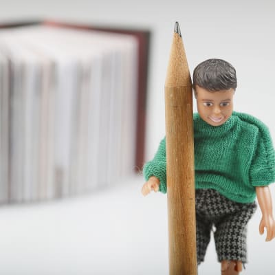 En docka som håller i en penna, framför en bok.