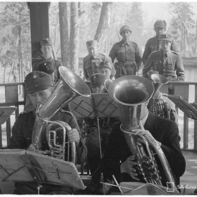 Militärklädda män spelar blåsinstrument på en terass. Bilden är gammal och svartvit.