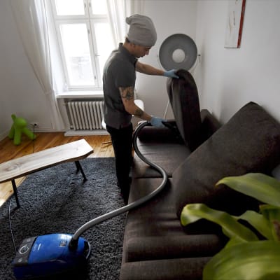 Städaren  Bayron Boloyi dammsuger soffan ett privat hem i Helsingfors i mars 2018. 