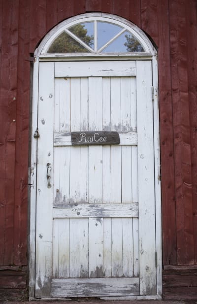 Ovessa kyltti PuuCee, Varjakansaaren vanhan sahakylän ulkohuussin ovi.