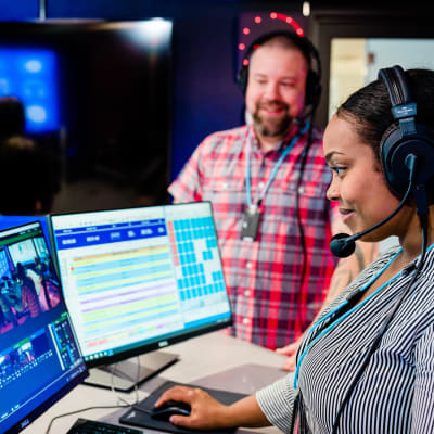 Kuvan etualalla nainen työskentelee radiostudiossa kuulokkeet korvillaan.