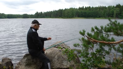 En äldre man metar vid en sjö.