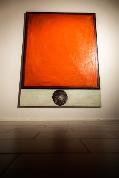 Röd målning upphängd och ljussatt mot en vit vägg