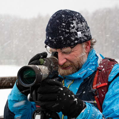Pontus Rancken tittar i sin tubkikare. Snön yr omkring honom.