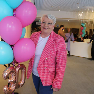 En person i rosa kavaj håller i ett knippe ballonger. 
