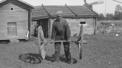 En man lyfter två kärrhjul. Bilden är tagen 1930 i Korsnäs.