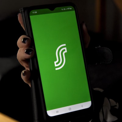 En hand håller i en mobiltelefon där S-bankens logotyp syns på grön botten.