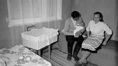 Mamma, pappa som håller i barnet i ett sparsamt möblerat rum på 50-talet kanske.