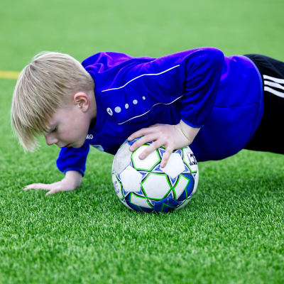 En pojke gör övningar på fotbollsträningar med blå jacka och svarta byxor. 