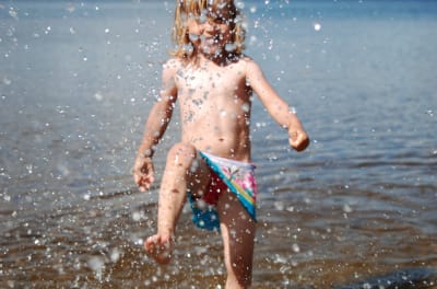 En flicka som plaskar i vattnet på en strand.