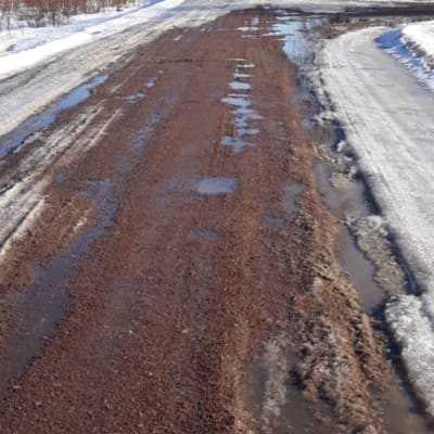 Kelirikon koettelema hiekkatie, jossa on jäätä ja vesilätäköitä.