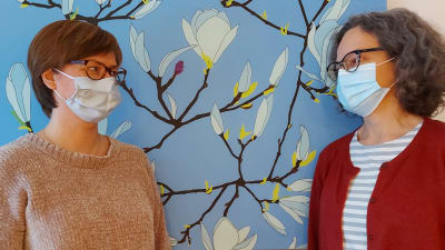 Johanna Björksten och sjukhusmusiker Anna Brummer stående intill en tavla i Johanna Björkstens vardagsrum. 2021.