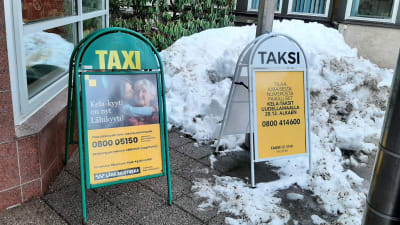Två skyltar med olika telefonnummer till olika taxicentraler.