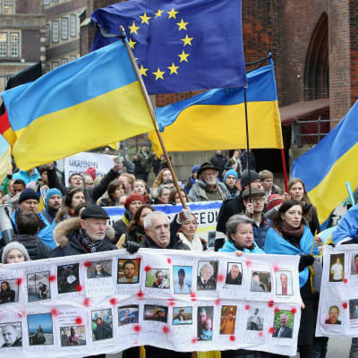 En bild på människor som går i ett demonstrationståg i Ukraina. Ukrainska flaggor syns i tåget.