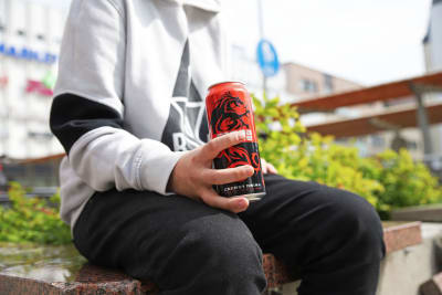 en ung flicka sitter ute med en energidryck i handen. 
