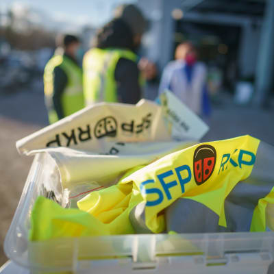 RKP:n vaalitapahtuma. Etualalla RKP:n vaalirekvisiittaa, taustalla kolme ehdokasta epäterävinä.