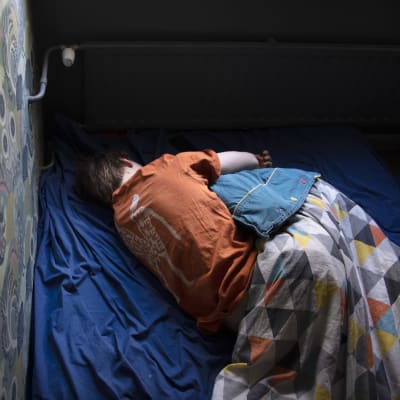 En ung människa ligger i sin säng. 