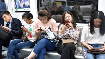 Kineser surfar på mobiltelefonen i ett tåg