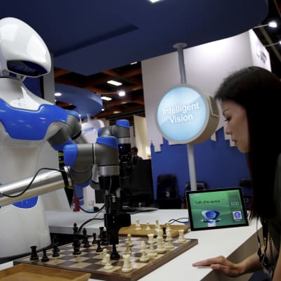 En vit robot spelar schack med en kvinna.