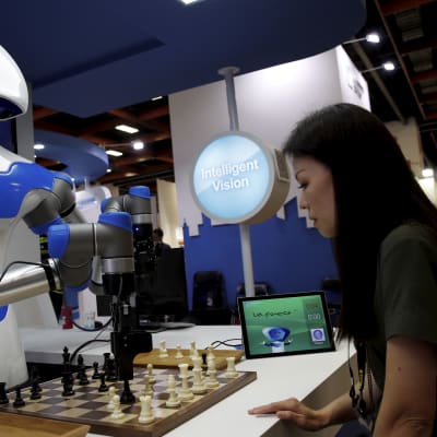 En vit robot spelar schack med en kvinna.