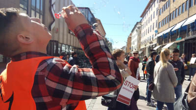 En person blåser såpbubblor på gågatan i Åbo och andra protesterar med skyltar mot Migrationsverkets beslut om avvisningar.