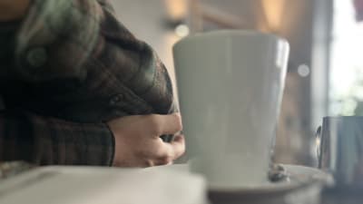 En hand, en arm och en vit kaffekopp.