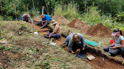 Personer sitter i ett sanddike på en arkeologisk utgrävning.