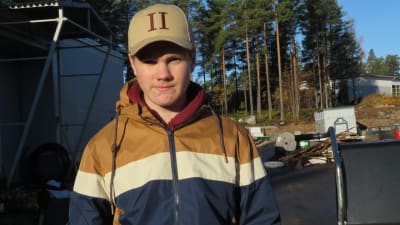 Valter Berglund, en ung man eller pojke står med ytterrock och keps står på en tomt där det byggs och finns ved.