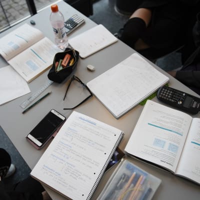 Ett bord fyllt med studietillbehör, häften, miniräknare och pennor. 