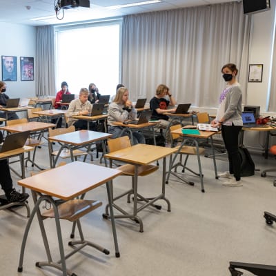Äidinkielen oppitunti Petäjäveden lukiossa. Oppilaat istuvat pulpeteissaan ja tekevät tehtävää tietokoneella. Opettaja seisoo luokan edessä.