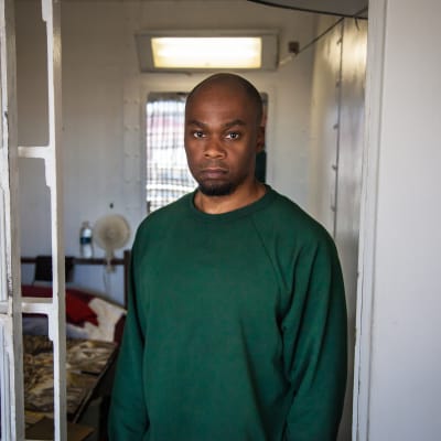 En intagen klädd i grön skjorta står vid gallret till sin cell i Atticafängelset i USA.