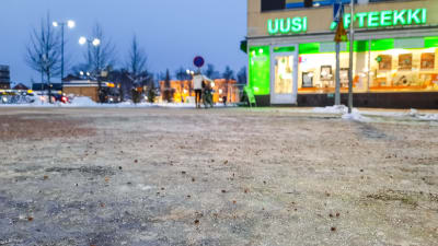 Person med cykel går över gatan i centrum av Borgå. Bilden är tagen nerifrån med fokus på den isiga marken närmast fotografen.