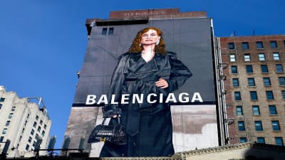 Isabelle Huppert pitkässsä takissa Balenciagakan mainoksessa joka on kiinnitetty talon seinään. Kuva on valtava.