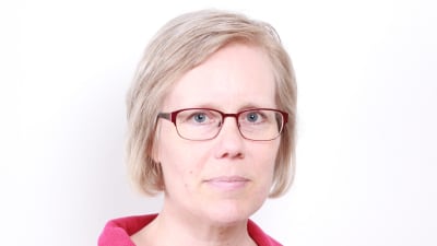 En kvinna i ljust hår och glasögon ser in i kameran.