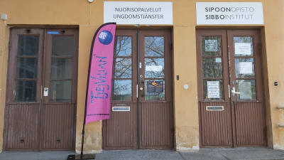 Tre ingångar till ett gult stenhus med olika trädörrar.  