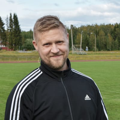 Mikael Kock iklädd sportdräkt tittar in i kameran. Idrottsplan i bakgrunden.