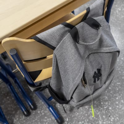 Yksinäinen koulureppu roikkuu luokassa tuolin selkänojasta.