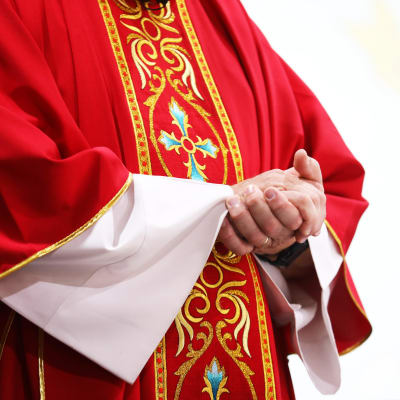 En katolsk präst i sin dräkt står och håller i händerna.