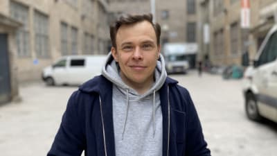 En leende man med mörkt hår och blå jacka.