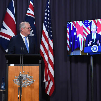 Australiens premiärminister Scott Morrison står och lyssnar på USA:s president Joe Biden som han talar med via videolänk. 