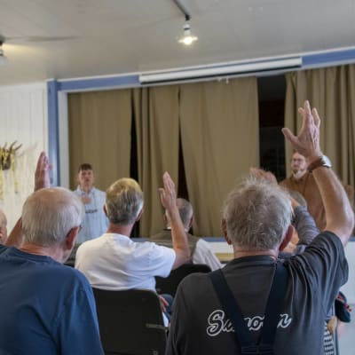 Många personer sträcker upp en hand på ett möte.