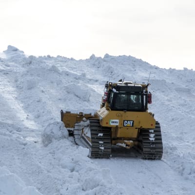En bandtraktor skuffar upp snön på snötippen i Borgå.