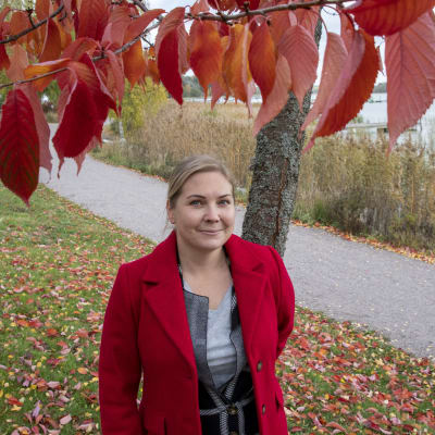 Jenny Högström har en röd jacka och står under ett träd med röda löv vid Hammars strand.